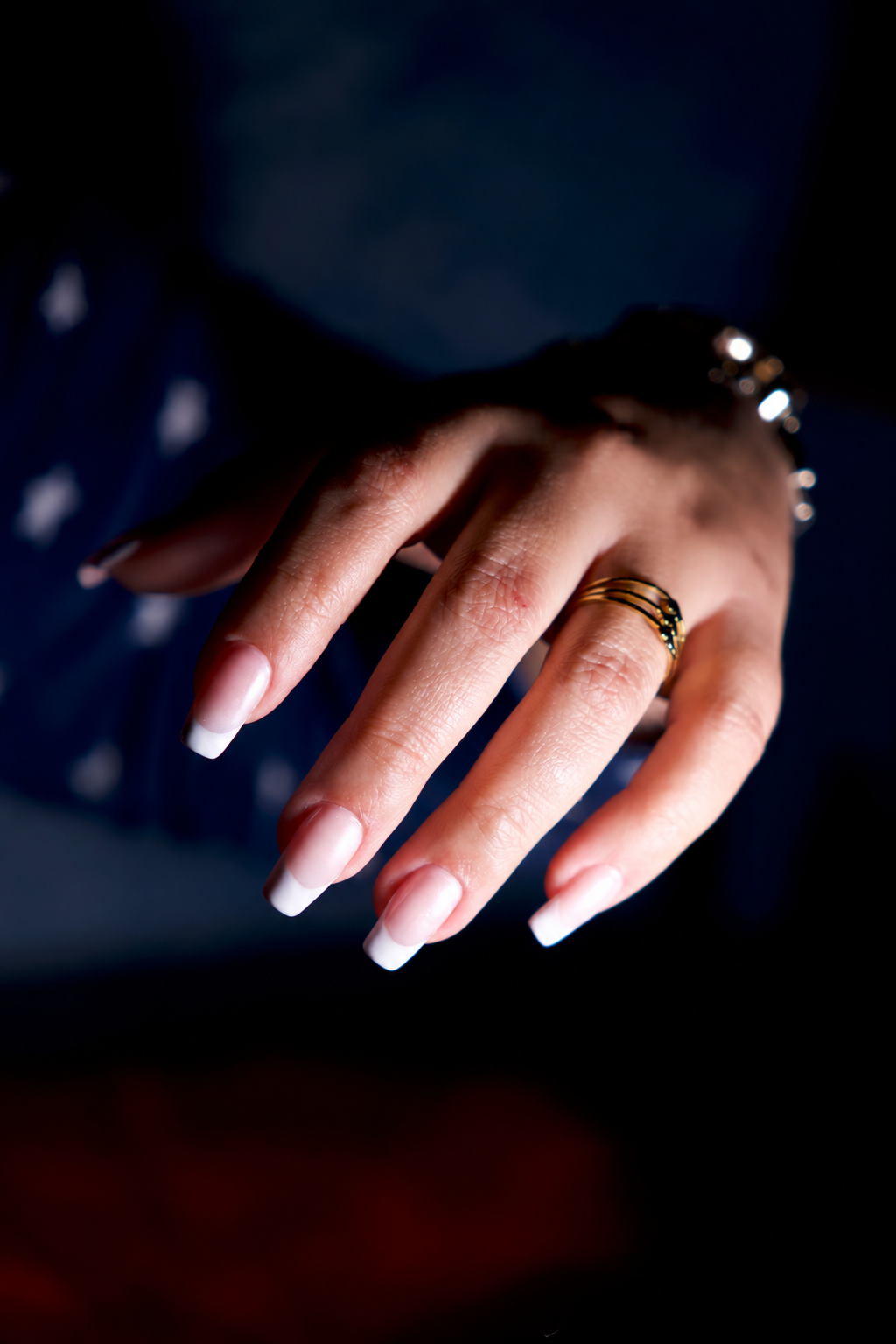 A hand with a French manicure, pale nails with white tips, and thin gold rings.