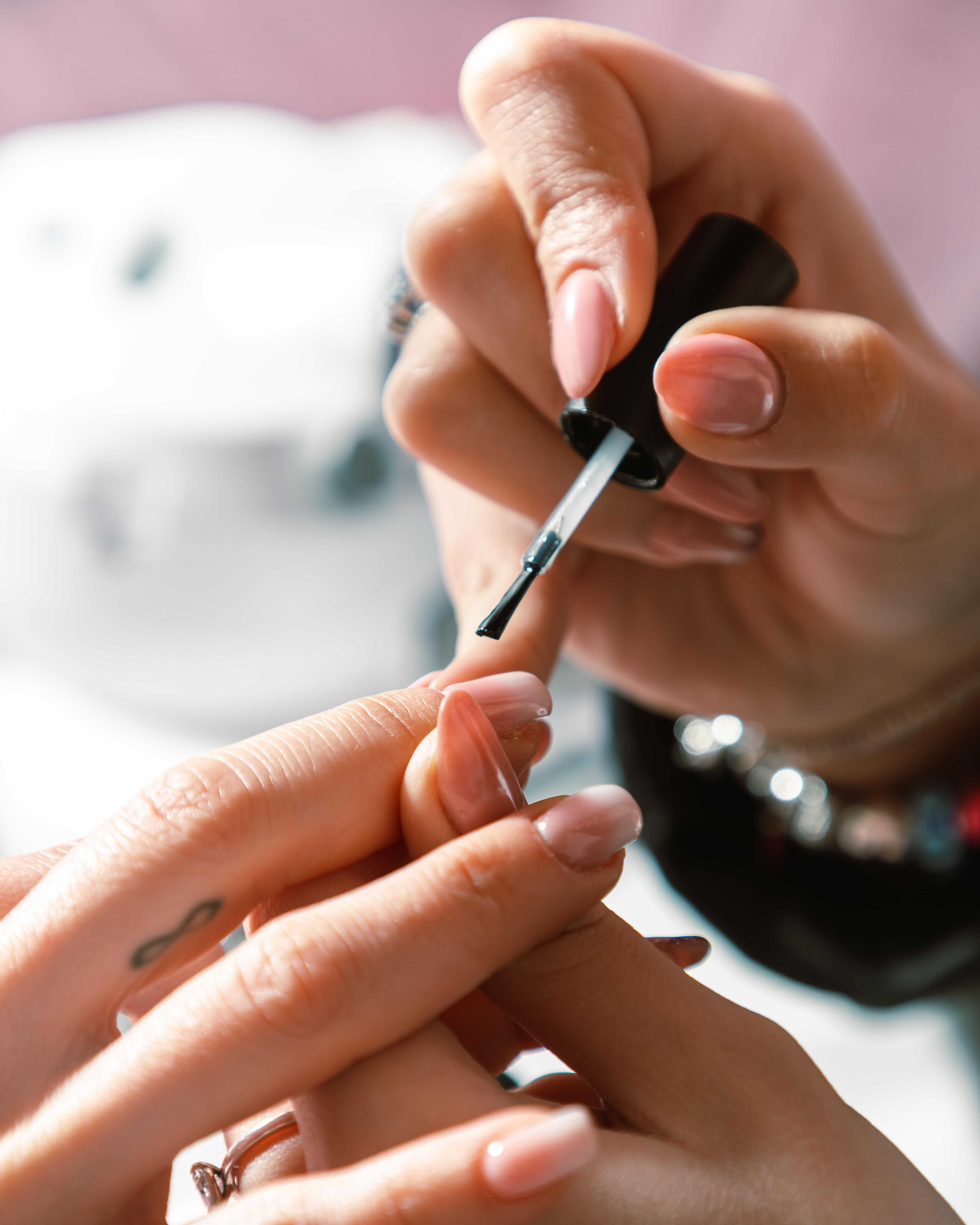 Hands brushing pale polish onto short natural nails.