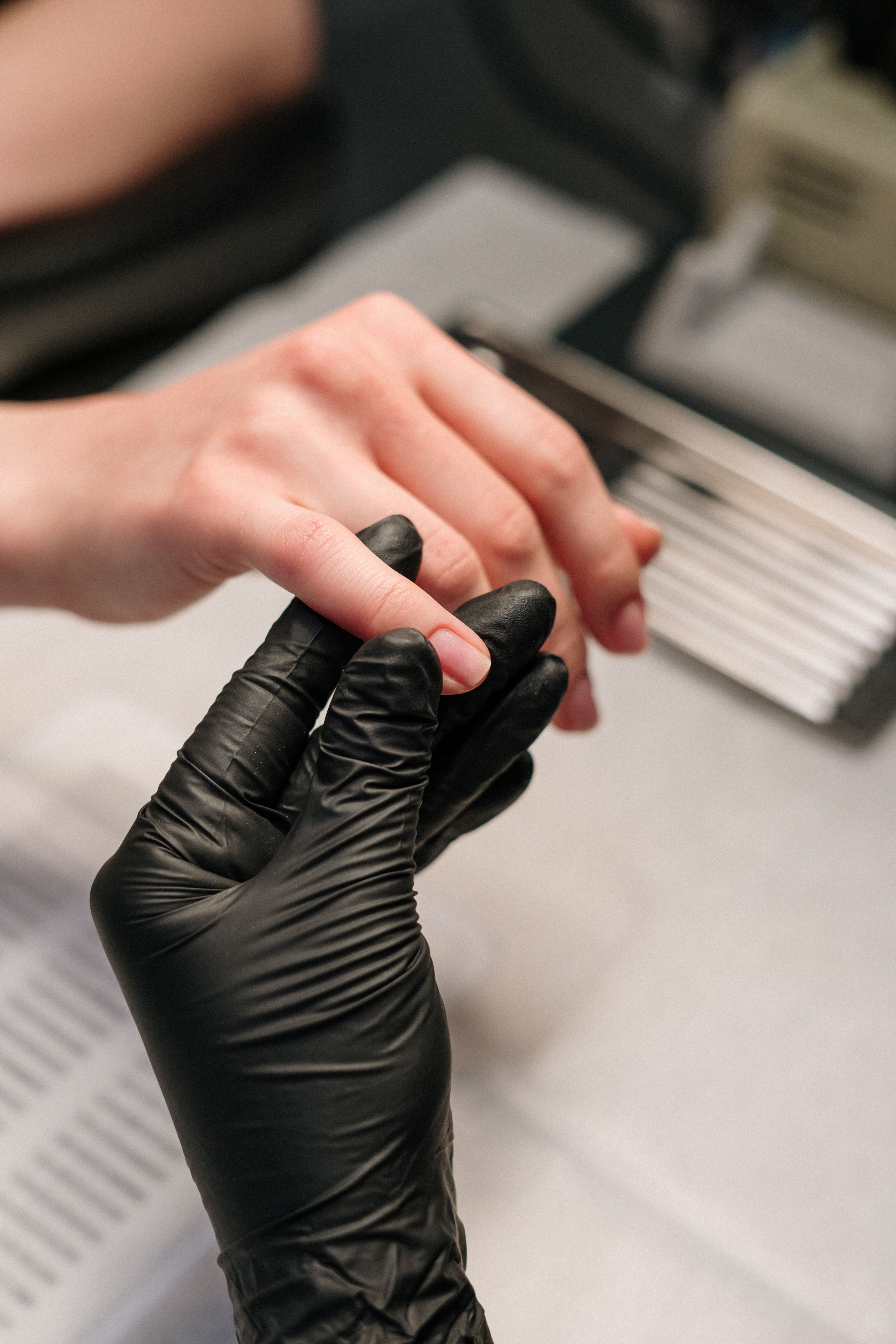 A gloved hand holding a finger with a short, unpolished nail, with metal files nearby.